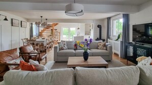 Una sala de estar amplia con sofá, mesa de centro y televisor. Una escalera conduce a un comedor con sillas y mesa.