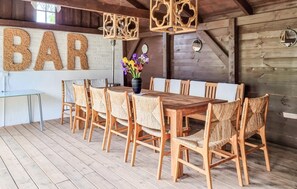 Un comedor rústico de madera con una mesa larga y sillas de mimbre, un cartel grande que dice 'BAR' y un jarrón con flores.