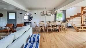 Amplia sala de estar con piso de madera, comedor con mesa y sillas redondas, una escalera y un espejo grande en la pared.