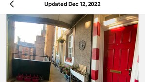 A corridor with a red door, a clock, and potted plants. - 2-bed Historic Apartment in old Town Edinburgh (Edinburgh)