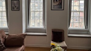 A room with a brown sofa, a chair with a cushion, and a poster on the wall. - 2-bed Historic Apartment in old Town Edinburgh (Edinburgh)