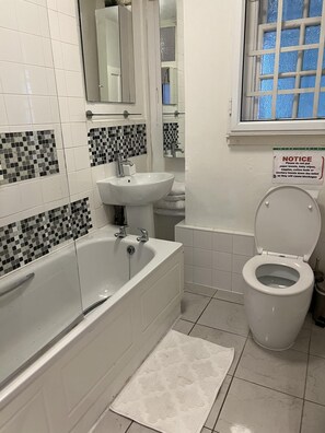 A bathroom with a bathtub, sink, and toilet. There is a notice on the wall about not putting paper towels down the toilet.