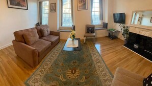 A living room with a brown sofa, a coffee table with flowers, a chair, a TV, and a fireplace. - 2-bed Historic Apartment in old Town Edinburgh (Edinburgh)