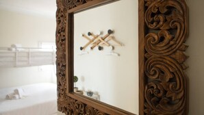Una habitación con un espejo grande y ornamentado, una cama con ropa blanca y un estante de pared con objetos de madera.