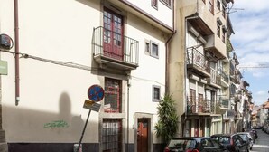 Una calle estrecha con autos estacionados, una puerta roja y un letrero que dice 'OBRAS'.