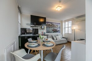A compact kitchen with modern appliances, a dining area with a round table and chairs, and a cozy living space with a sofa and a large window.