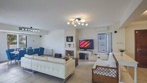 A modern living room with a white sofa, dining table with blue chairs, a TV, and a fireplace. - Protaras Serifos Villa Sv07 (Paralimni)