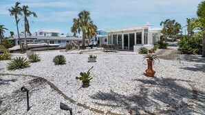 Una casa moderna con un patio que presenta piedras blancas, plantas en macetas y un muelle para embarcaciones.