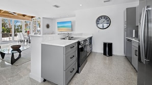 Una cocina moderna con una isla grande, electrodomésticos de acero inoxidable y vistas a la playa a través de amplios ventanales.