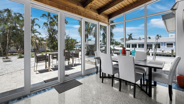 Un área de comedor al aire libre techada, con vista a palmeras y una playa.