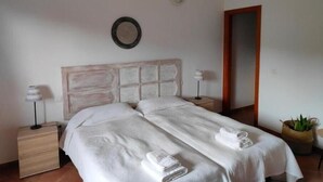Une chambre d’hôtel avec un grand lit, deux tables de chevet, un miroir et une plante en pot.