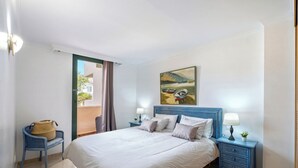Une chambre à coucher avec un lit, une table de chevet, une chaise, une fenêtre avec des rideaux et un tableau accroché au mur.