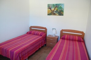 Une petite chambre propre, avec deux lits simples, une table de chevet avec une lampe et un tableau au mur.