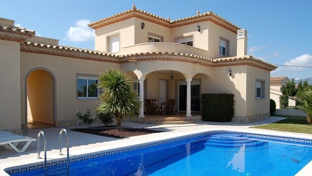 Une maison à deux étages avec une piscine, une terrasse avec des chaises et un petit jardin.