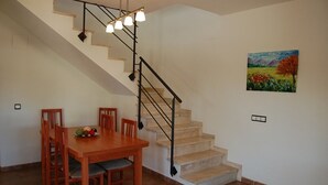 Un coin repas avec une table et des chaises en bois, un escalier avec une rampe noire et un tableau accroché au mur.
