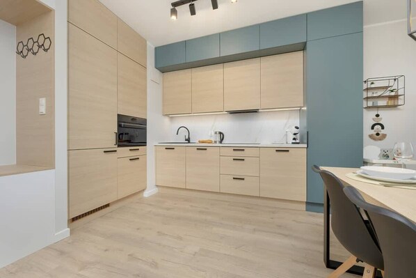 Una cocina moderna con armarios de madera clara, una isla central y una zona de comedor con mesa y sillas.
