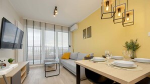 Una sala de estar moderna con un sofá, una mesa de comedor para dos personas y un televisor montado en la pared.