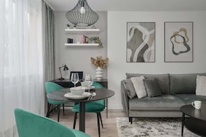 Una sala de estar moderna con un sofá gris, sillas color turquesa, una mesa de comedor con una lámpara negra y arte abstracto en la pared.