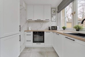 Una cocina moderna con armarios blancos, horno empotrado, microondas y ventana con vistas al exterior.