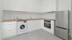 A modern kitchen with white cabinetry, a washing machine, an oven, and a refrigerator. - Stylish Studio near the Fair | Private Parking (Poznan)