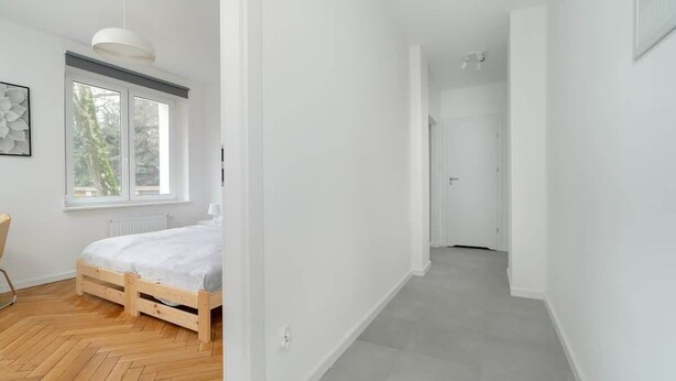 A modern bedroom with a wooden bed, a large window, and a hallway leading to another room. - Stylish Studio near the Fair | Private Parking (Poznan)