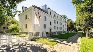 A multi-story building with a white facade, a flag, and a paved pathway. - Stylish Studio near the Fair | Private Parking (Poznan)