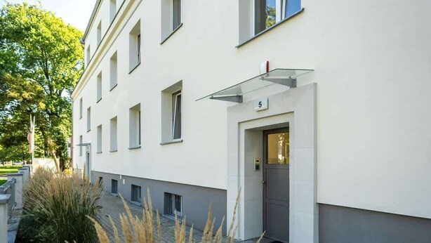 A modern building with a flat facade, numbered 5, featuring a glass entrance canopy and a small entryway. - Functional Studio in Poznan | Parking, SmartTV (Poznan)