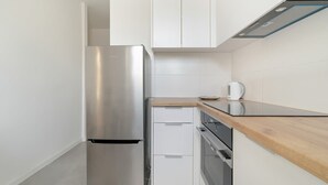 A compact kitchen with a stainless steel refrigerator, white cabinets, a wooden countertop, and a built-in oven. - Functional Studio in Poznan | Parking, SmartTV (Poznan)