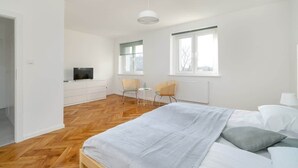 A modern bedroom with a large bed, a TV on a white cabinet, two chairs, and a window. - Functional Studio in Poznan | Parking, SmartTV (Poznan)