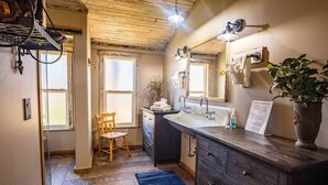 Un baño con tocador de madera, un espejo grande, un lavamanos y una silla.