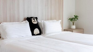 A neatly made bed with white bedding, a black and white pillow, and a small potted plant on a bedside table. - Bears Den Pattaya (Pattaya)