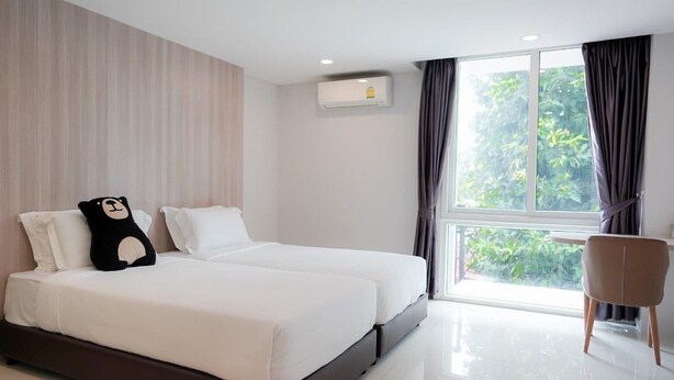 A modern hotel room with a large bed, a chair, and a window with curtains. - Bears Den Pattaya (Pattaya)