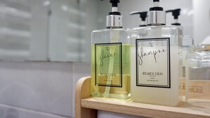 Two bottles of 'Shower' and 'Bear's Den' shampoo on a wooden shelf in a bathroom. - Bears Den Pattaya (Pattaya)