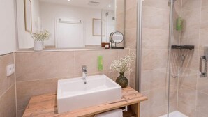 Een moderne badkamer met een witte wastafel, een douchecabine van glas en een spiegel boven de wastafel.
