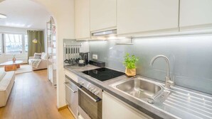 Een moderne keuken met een ingebouwde kookplaat, spoelbak en oven. Er is een zithoek met een witte bank en een tafel.