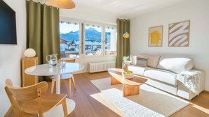 Een moderne woonkamer met een witte bank, een houten salontafel en een eethoek met een witte tafel en stoelen.