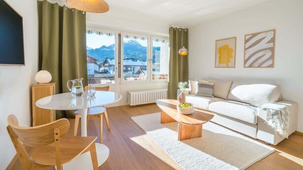Een moderne woonkamer met een witte bank, een houten salontafel en een eethoek met een witte tafel en stoelen.