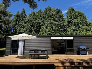 Eine moderne Außenpatio mit Holzboden, einer Bank, einem Grill und einem überdachten Sitzbereich mit Sonnenschirm.