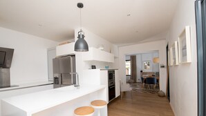 Et moderne køkken med lyse skabe, en central ø med barstole og en hængende pendel.