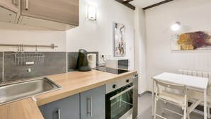A compact kitchen with a sink, stove, and microwave. There is a small dining area with a table and chairs.