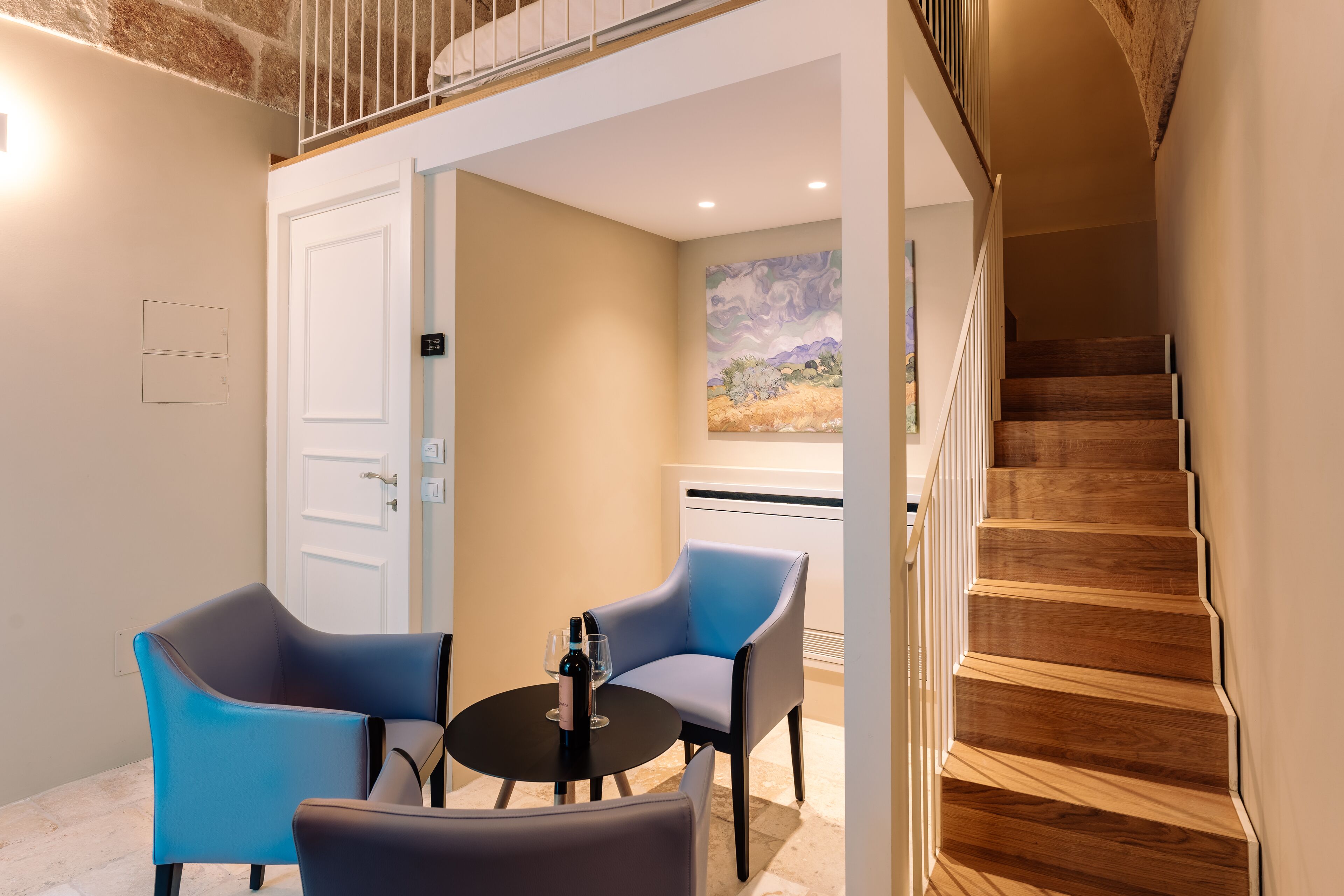 Una habitación moderna con una escalera de madera, una zona de comedor con dos sillas y una mesa, y un cuadro en la pared.