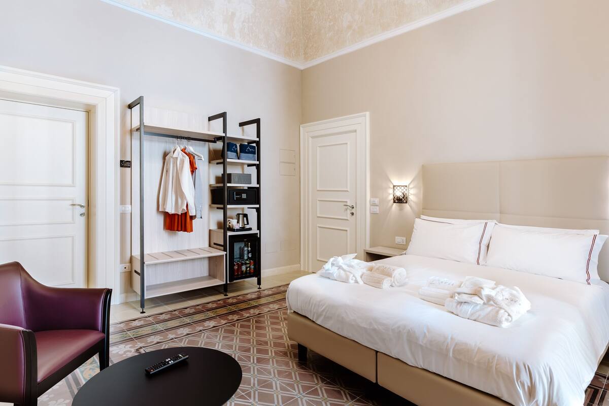 A hotel room with a bed, a seating area, a wardrobe, and a small table.