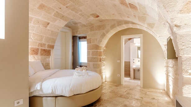 A bedroom with a round bed, stone walls, and a view of a bathroom. - Aeris Suite & Relax (Polignano a Mare)