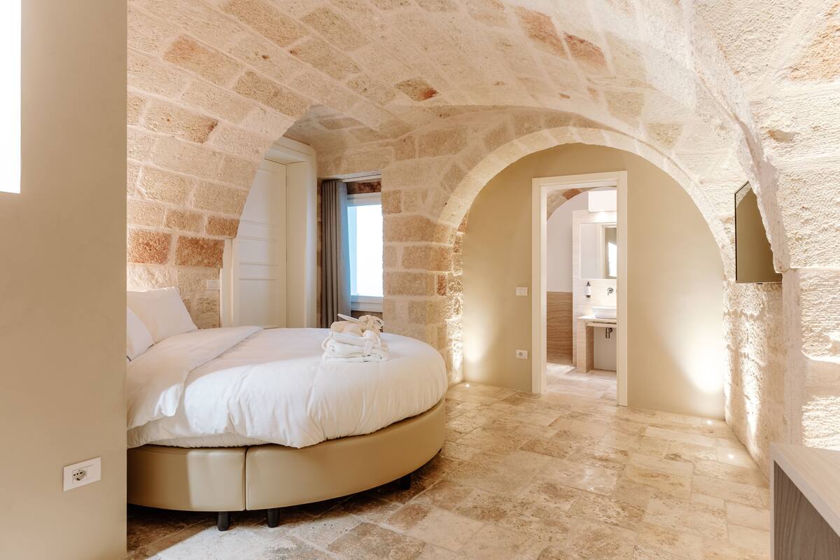 A bedroom with a round bed, stone walls, and a view of a bathroom.