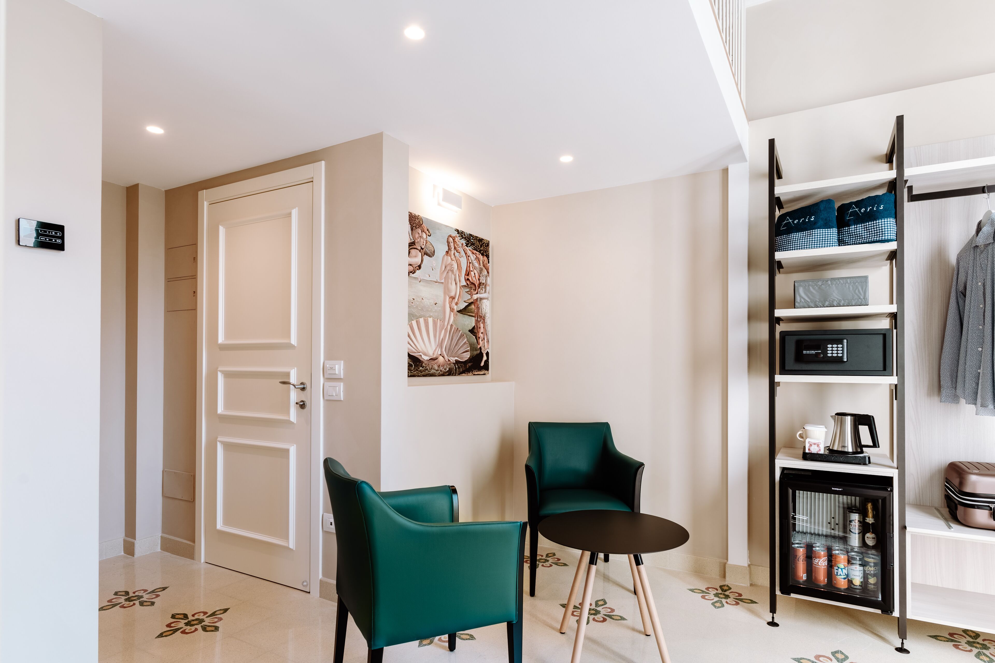 A modern room with teal chairs, a small table, a wall-mounted shelf with storage, and a door leading to another area.