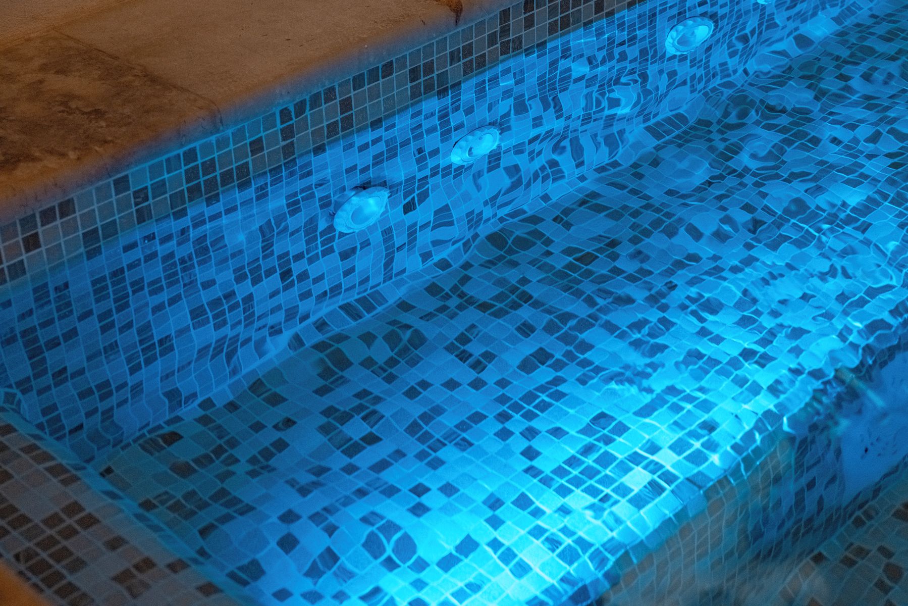 Une piscine avec un bord carrelé et un éclairage bleu.