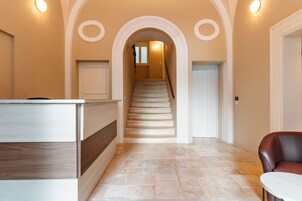 Un pasillo amplio con una escalera que conduce a un segundo piso, un mostrador de recepción y una zona de estar.