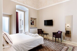 Ein Hotelzimmer mit einem großen Bett, einem Flachbildfernseher, einer Sitzecke mit zwei Sesseln und einem Spiegel an der Wand.