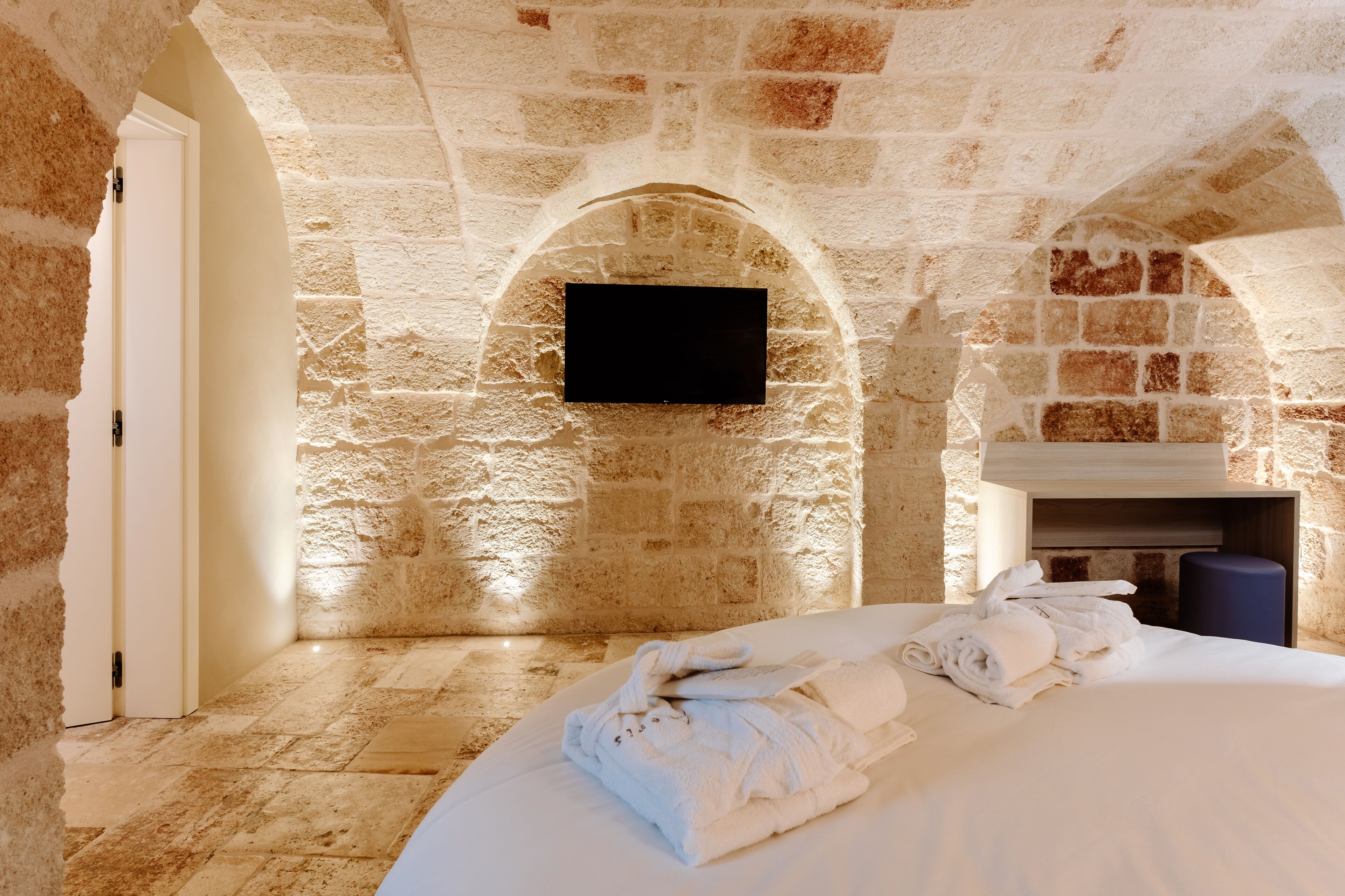 Een kamer met stenen muren, een bed, een flatscreen televisie en een open haard.