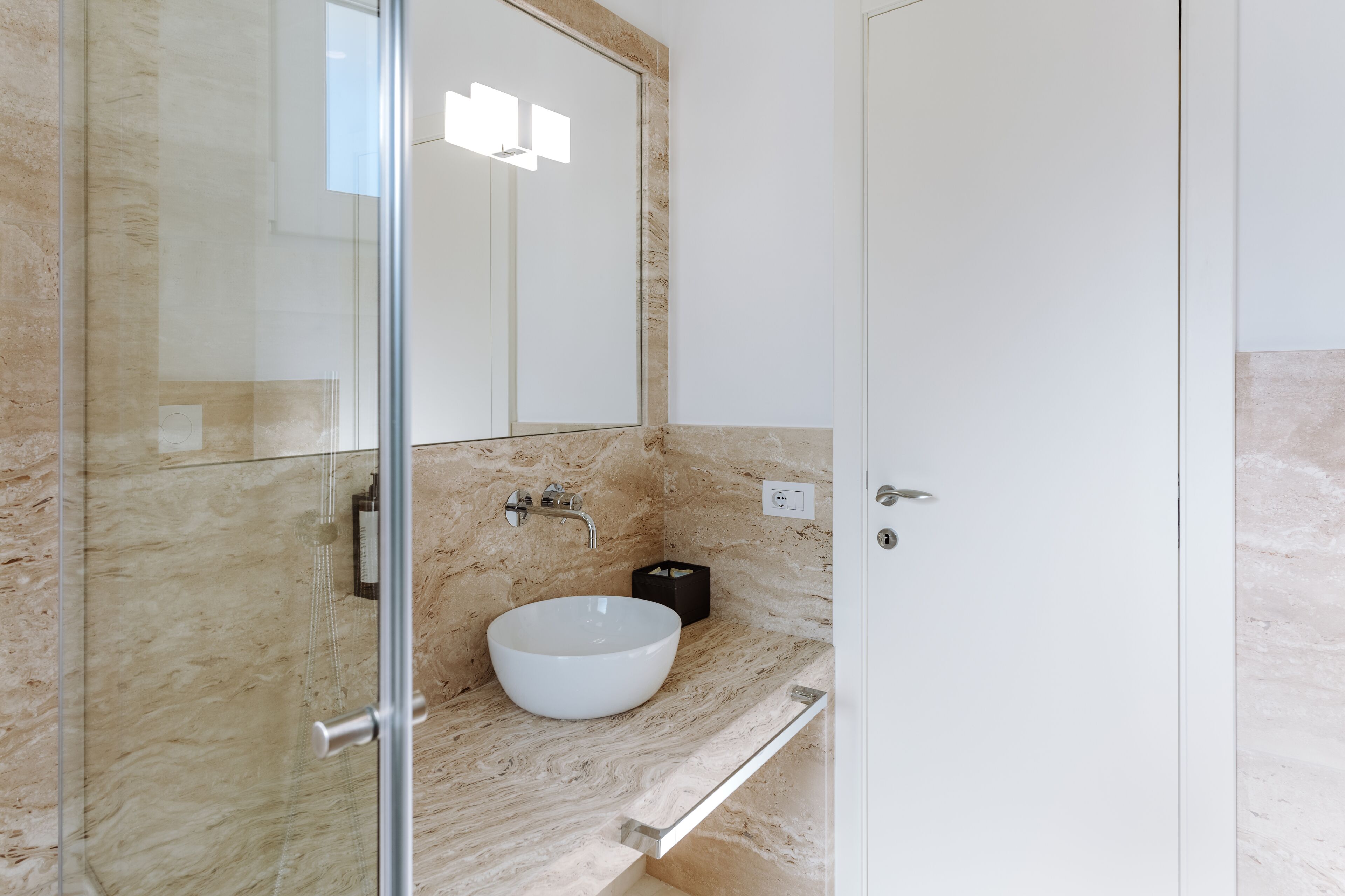 A modern bathroom with a glass shower enclosure, a white sink, and a marble countertop.